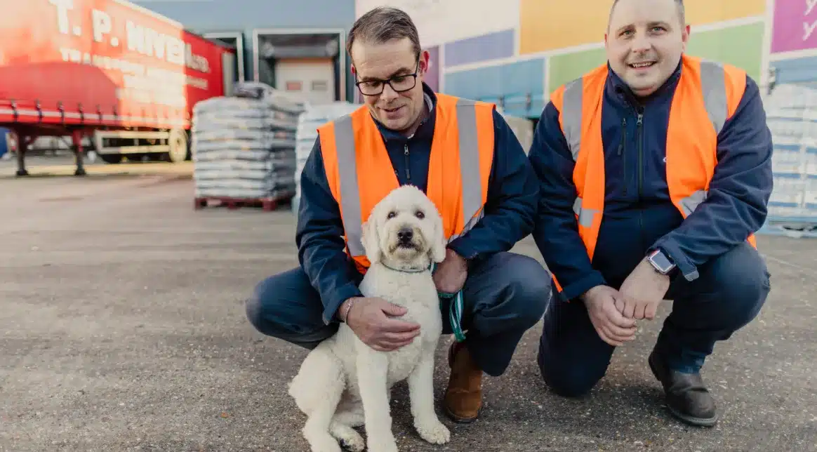Image shows Macfarlane Packaging logistics staff posting with a cockerpoo in front of Macfarlane trucks